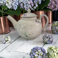 Decorative teapot with floral  and dragonfly patterns on a white wooden surface with hydrangeas.